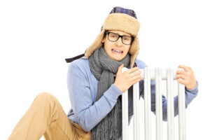 hilled young man with winter hat sitting next to a radiator isolated on white background